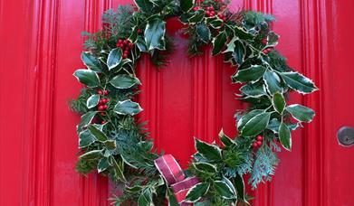 A green leafy Christmas wreath hanging on a red door