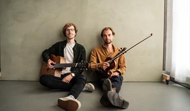 A young guitarist and a young fiddle player sitting on the floor holding their instruments