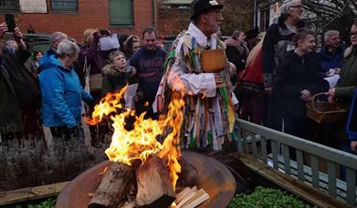 A large group of people singing in front of a log fire outdoors