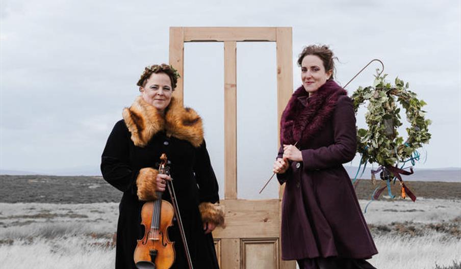 A woman holding a violin and a woman holding a guitar in a snowy field.